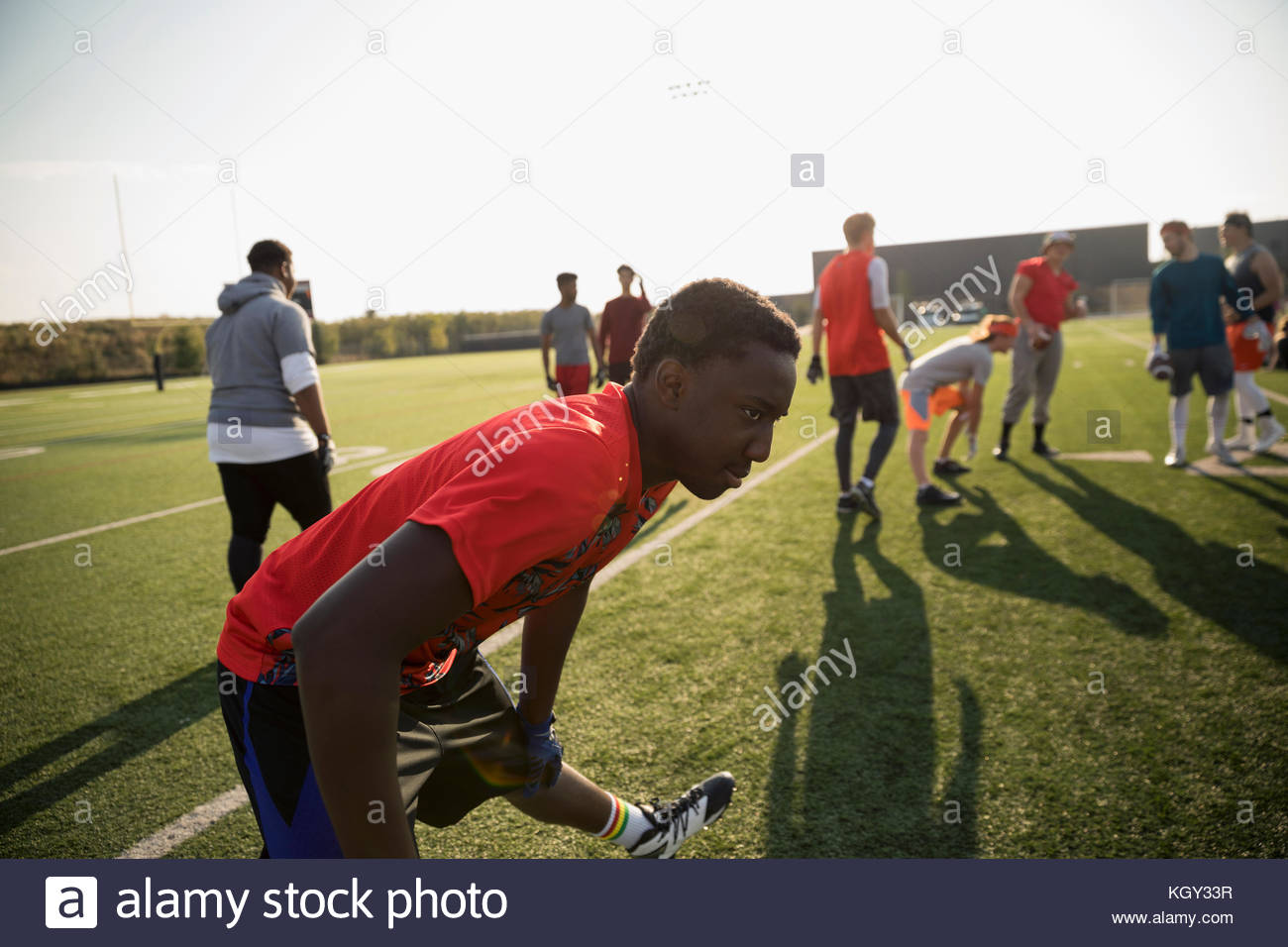 Teenage boy high school football player stretching leg on sunny football field Stock Photo