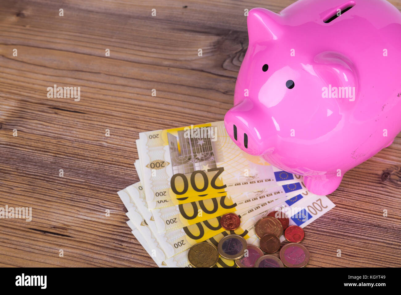 Piggy bank with stack of two hundred euro banknotes and coins on wooden ...