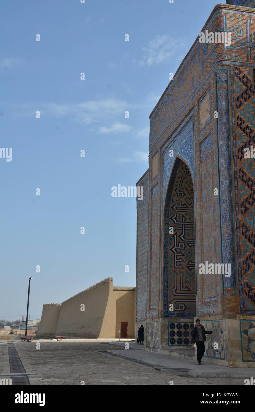 Man and woman walking next to facade touching wall. Turkestan is an ancient city, Kazakhstan. Many mausoleums; Khwaja Ahmad Yasavi Stock Photo