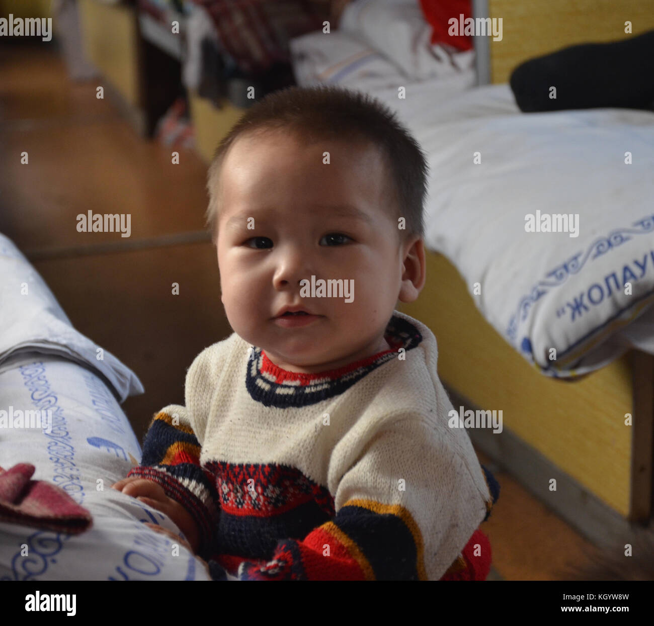 little cute Kazakh baby boy with Asian with cockeyed eyes staring to someone with open mouth wearing a winter wool sweater. Stock Photo