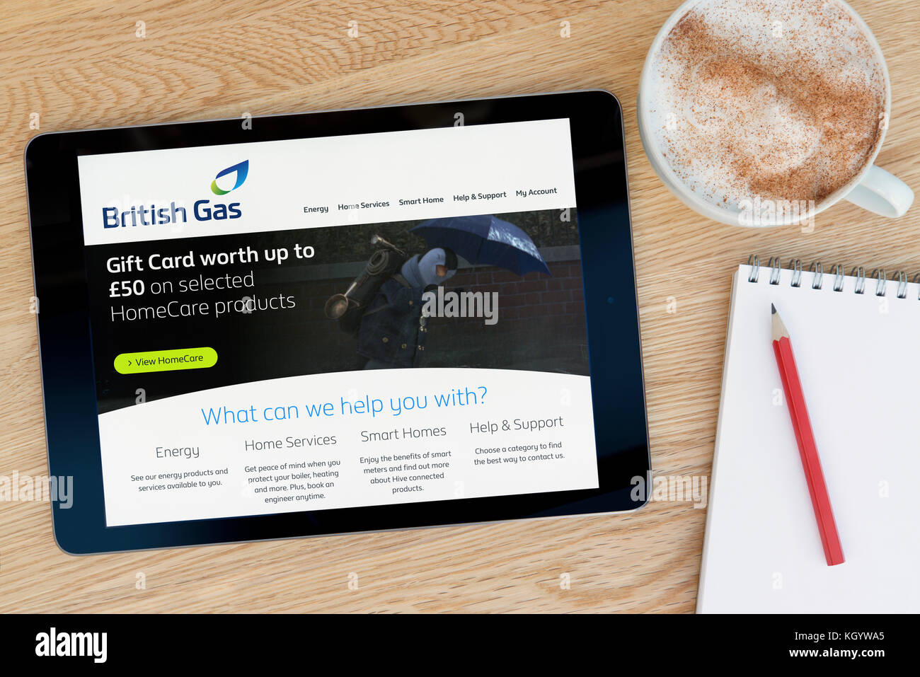 The British Gas website features on an iPad tablet device which rests on a wooden table beside a notepad & pencil and a cup of coffee (Editorial only) Stock Photo