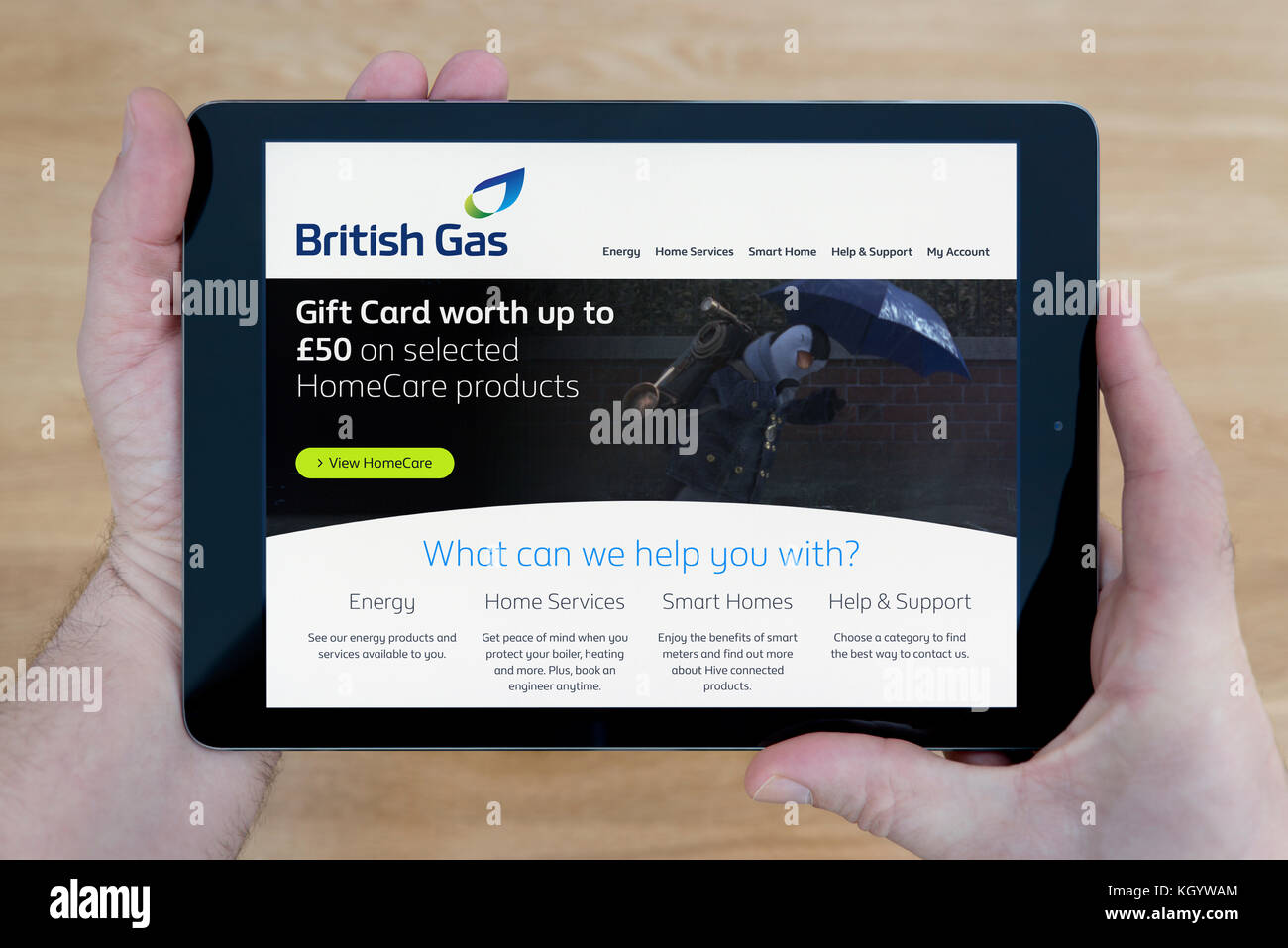 A man looks at the British Gas website on his iPad tablet device, shot against a wooden table top background (Editorial use only) Stock Photo