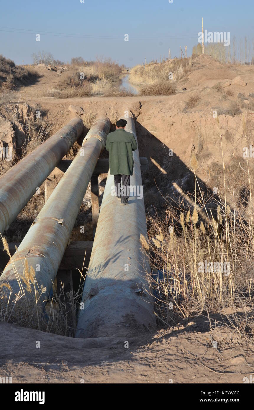 Old man with jacket and cap walking over a huge pipe in the ground