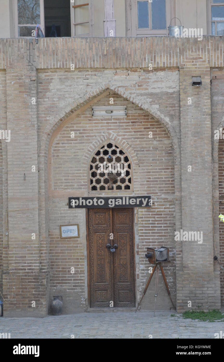 An old fashioned camera on tripod standing in front of a photo gallery in Bukhara, Uzbekistan. Old carved with islamic pattern wooden door is locked. Stock Photo