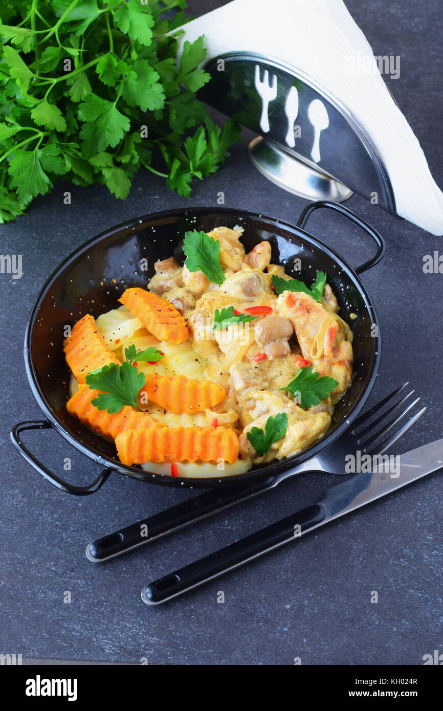 Chicken fillet with mushrooms in a creamy sauce and fried sweet potato in a black metal bowl on a grey abstract background. Healthy eating concept Stock Photo