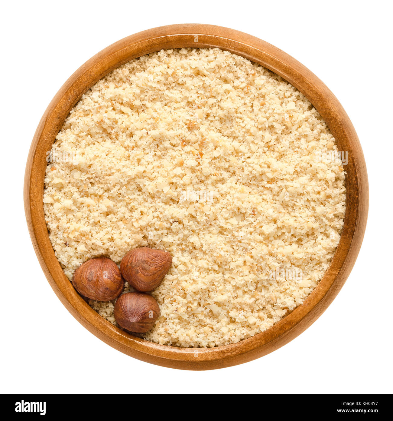 Three shelled hazelnuts on hazelnut meal in wooden bowl. Grounded nuts of hazel, Corylus avellana, also called cobnut or filbert nut. Stock Photo