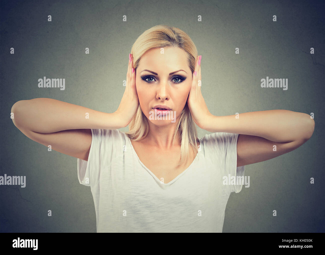 Portrait of young woman covering with hands her ears, isolated on gray background Stock Photo