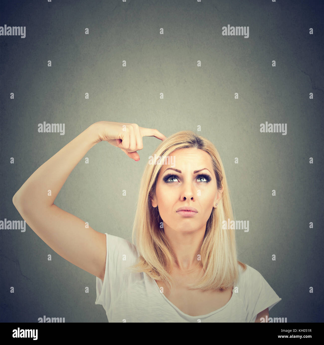 Portrait of a thinking woman bewildered scratching her head seeks a solution looking up isolated on gray wall background. Stock Photo