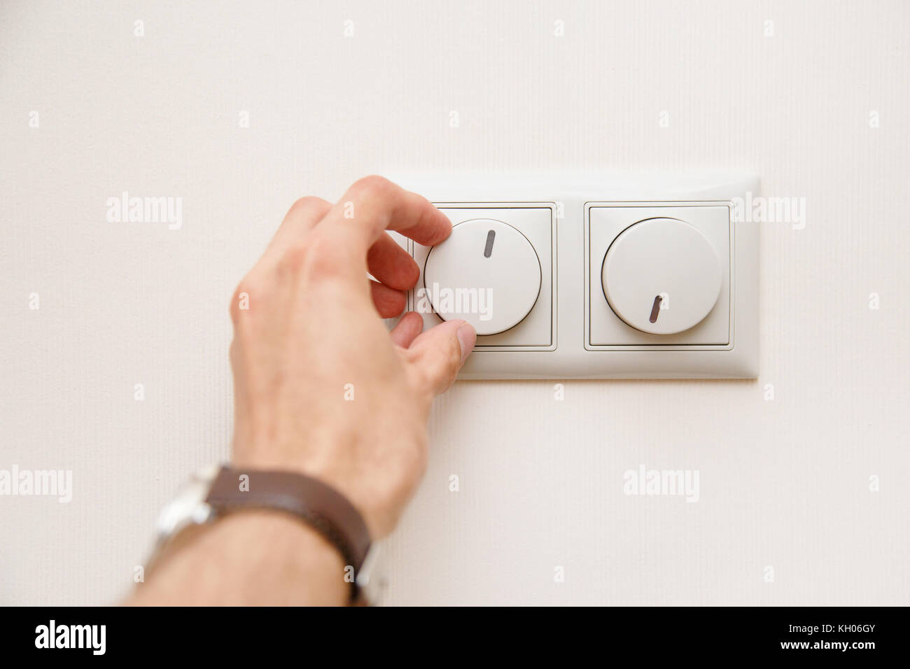 Saving energy concept: Human hand turning down electrical light dimmer switch or conditioner heat controller Stock Photo