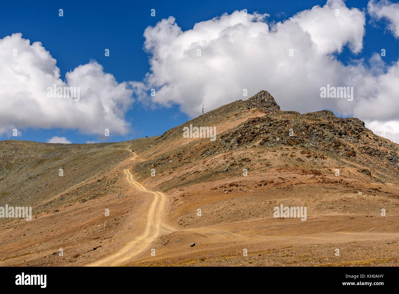 Scenic view with the winding gravel road to the top of the mountain on a background of blue sky and clouds on a sunny day Stock Photo