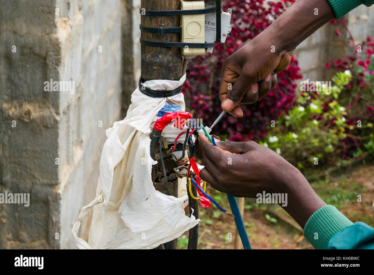 African male electrician working on hazardous looking exposed electrical cables outdoors, Kenya, East Africa Stock Photo
