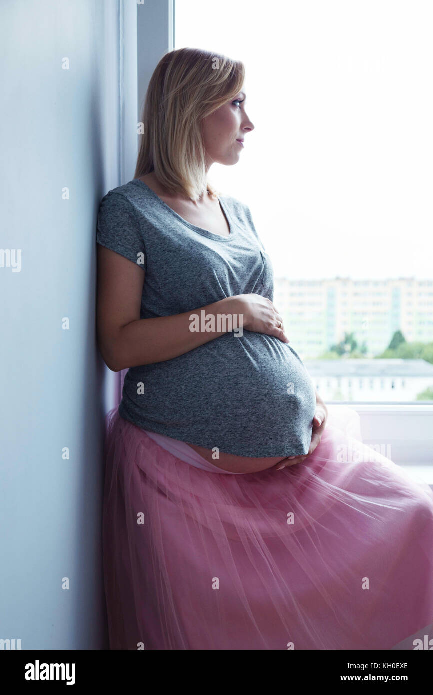 Momtobe sitting on a window sill in a pink skirt and a tshirt