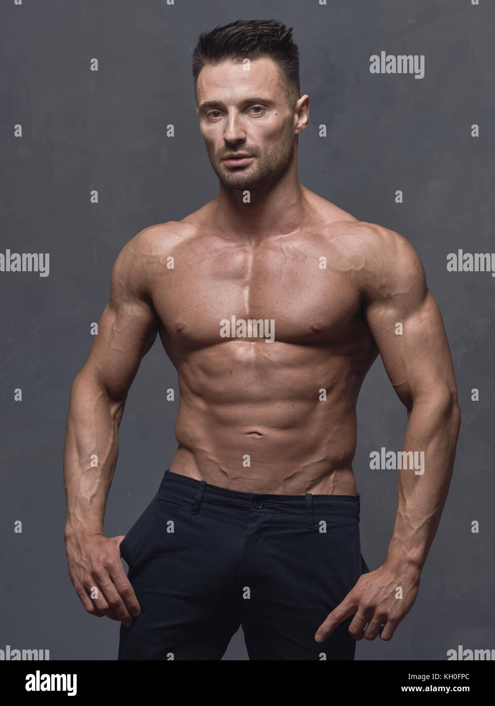 A black-haired man with a short haircut is standing near the gray textured  wall. The guy has strong muscular arms and shoulders. His body is bare to t  Stock Photo - Alamy
