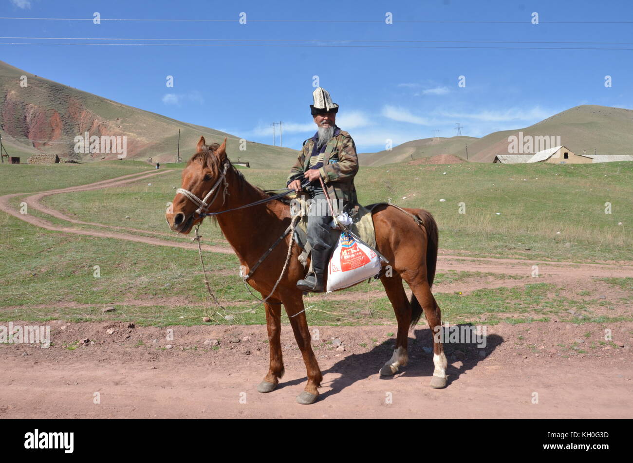 A Kyrgyz man, wearing a traditional kalpak hat, riding a horse in Kyrgyzstan, central Asia. Stock Photo