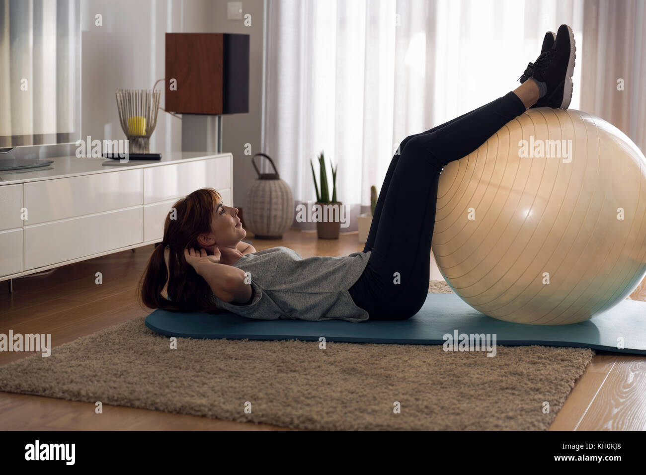 Full length shot of a woman doing exercise at home with a swiss Ball ...