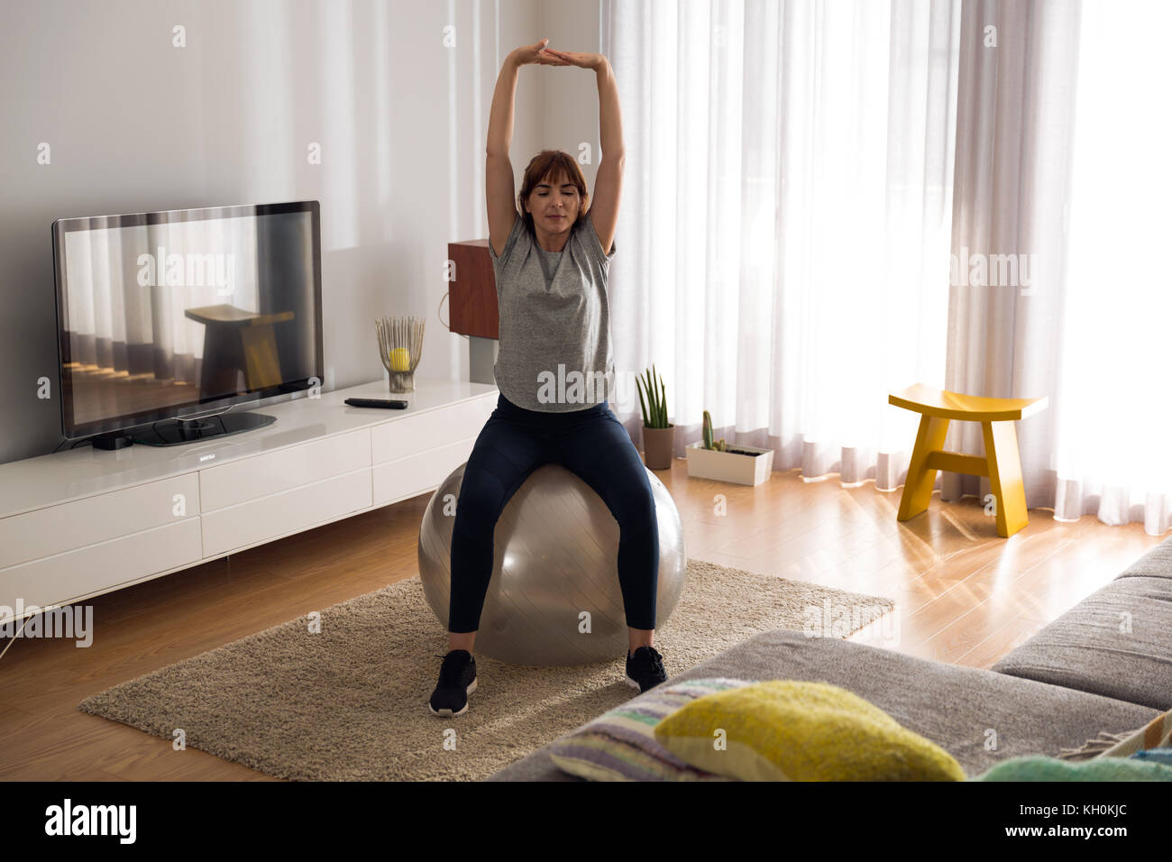 Full length shot of a woman doing exercise at home with a swiss Ball ...