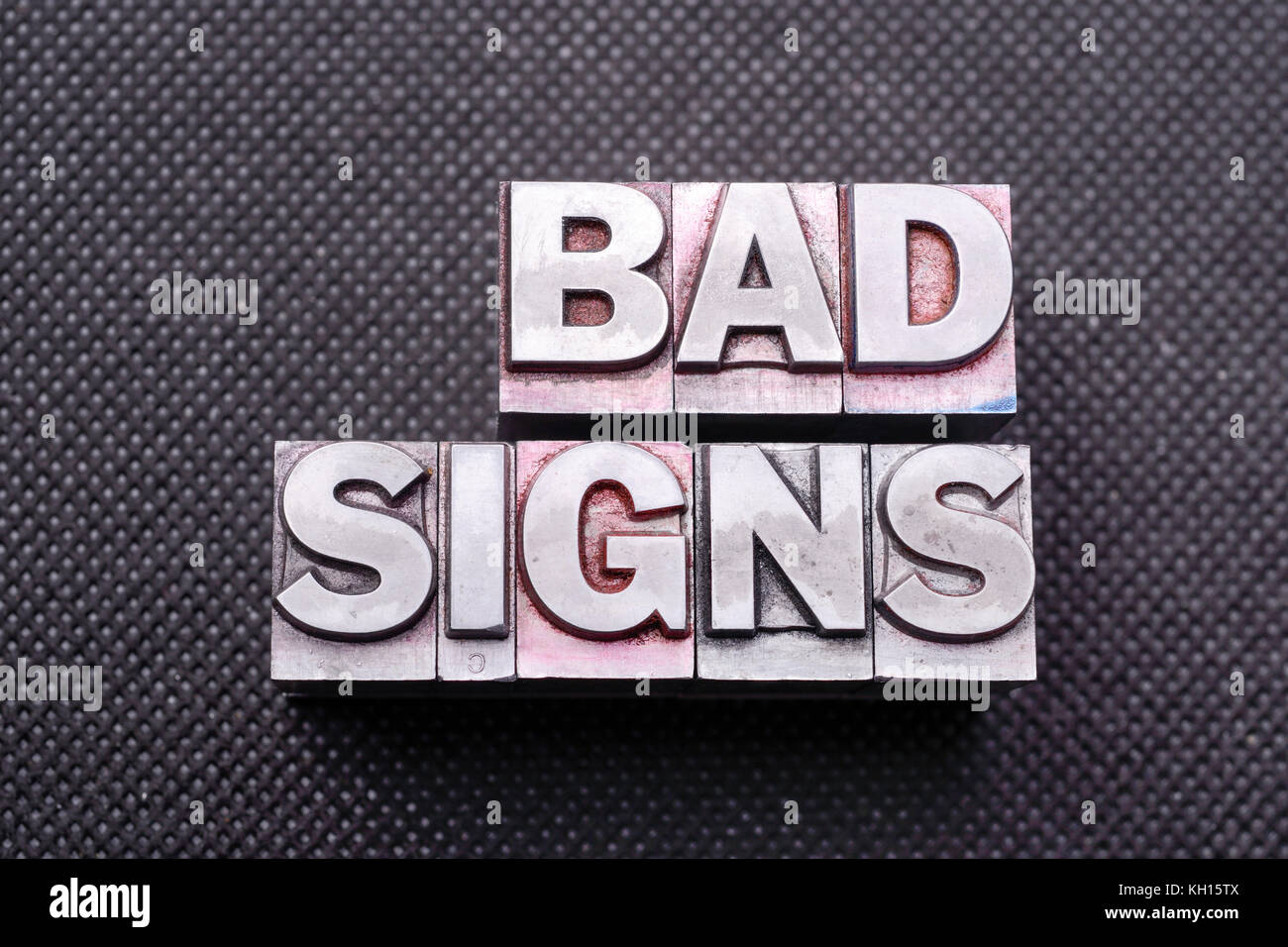 bad signs phrase made from metallic letterpress blocks on black perforated surface Stock Photo