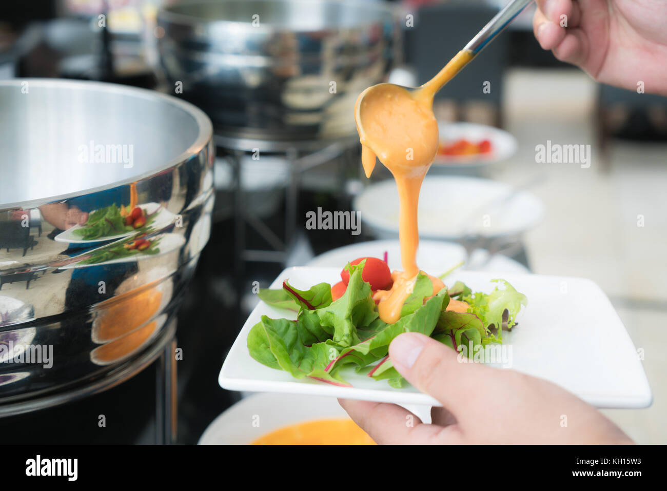 Tablespoon measure of creamy thousand island dressing being poured over fresh garden salad in breakfast buffet at hotel. Stock Photo