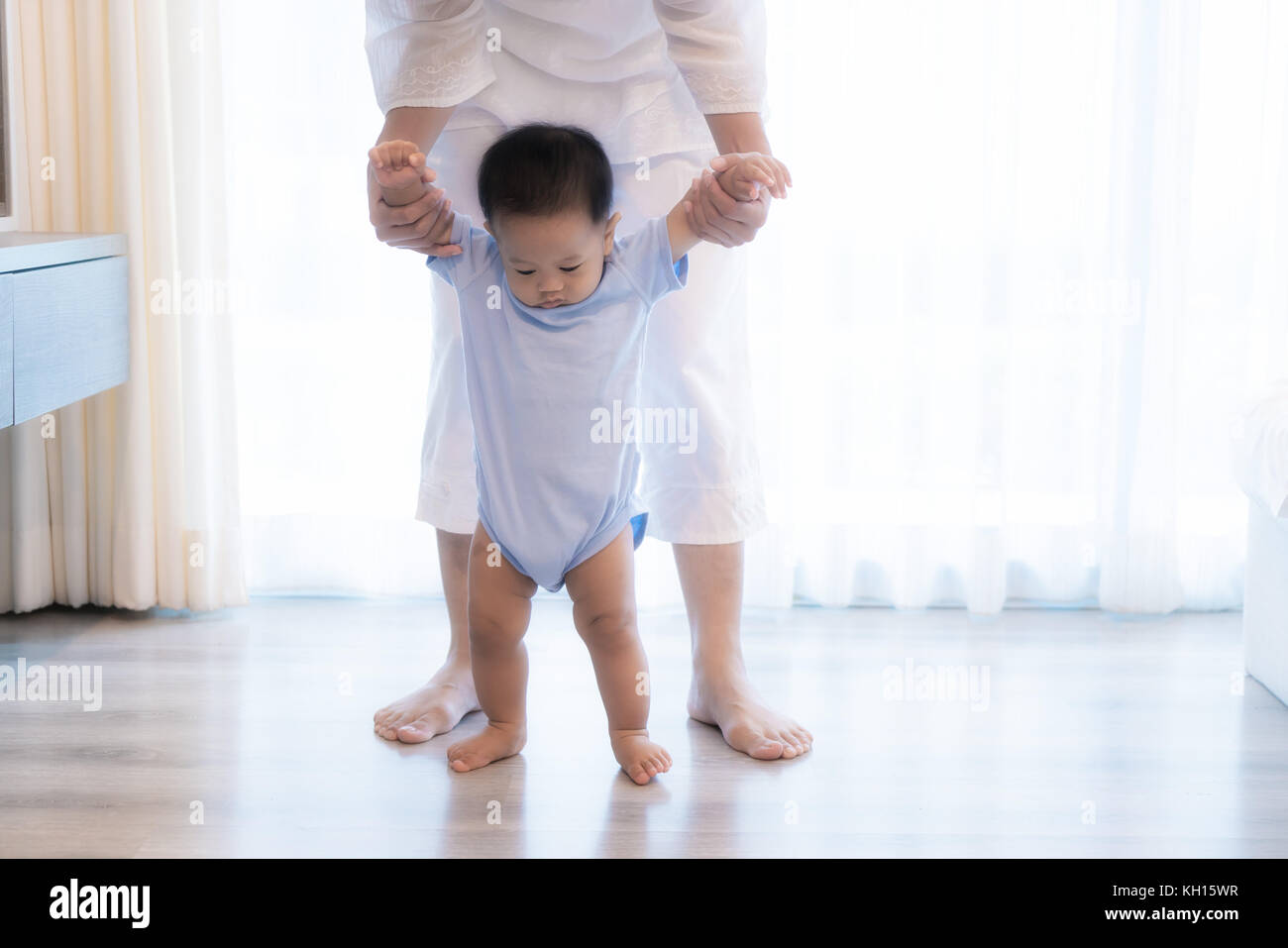 Happy Asian little baby boy learning to walk with mother help in bedroom at home. Family, child, childhood and parenthood concept Stock Photo