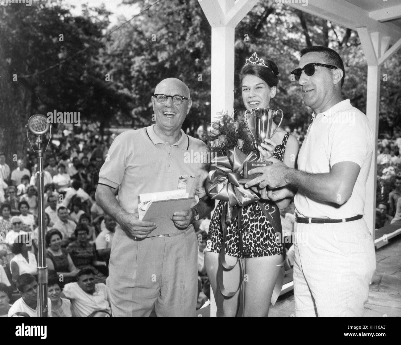 The unnamed winner of the Miss Interior Beauty Pageant (center) is presented with a bouquet and trophy by an unnamed man (left) and Secretary of the Interior Stewart Udall (right). July 28, 1962. Photo by Abbie Rowe. Stock Photo