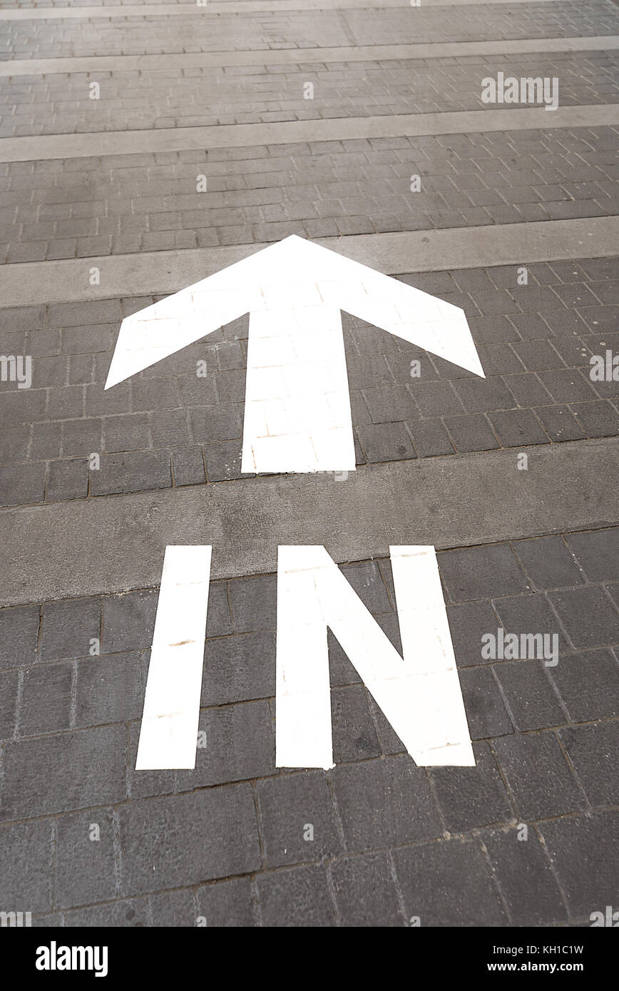 A bright white directional arrow and the word ‘IN’ painted on a road way entrance. Stock Photo
