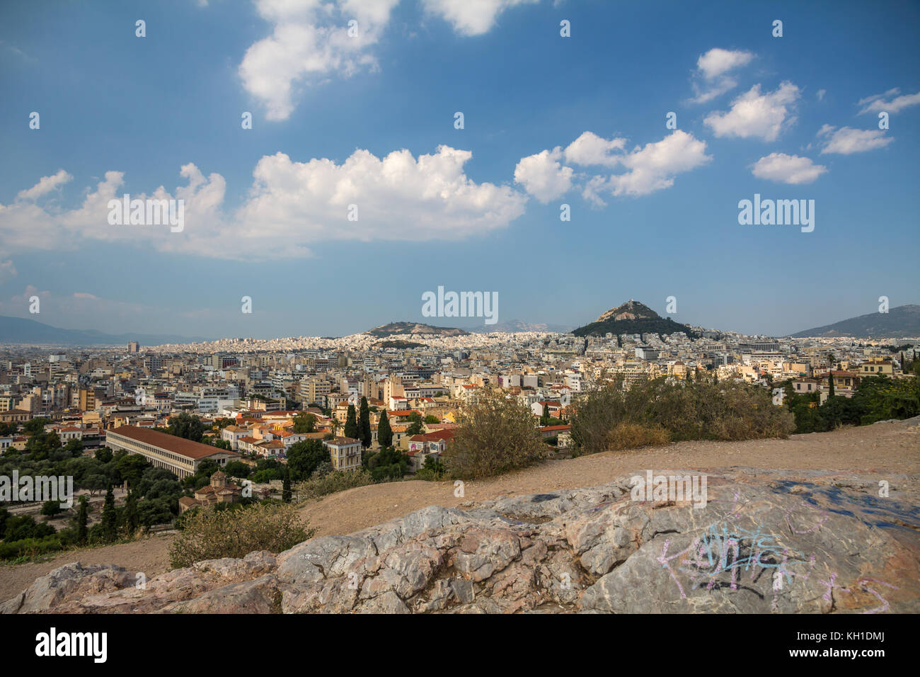 The City of Athens spreads out below Mars Hill where rocks in the foreground have been adorned by grafitti.  Light white clouds float in the azure blu Stock Photo