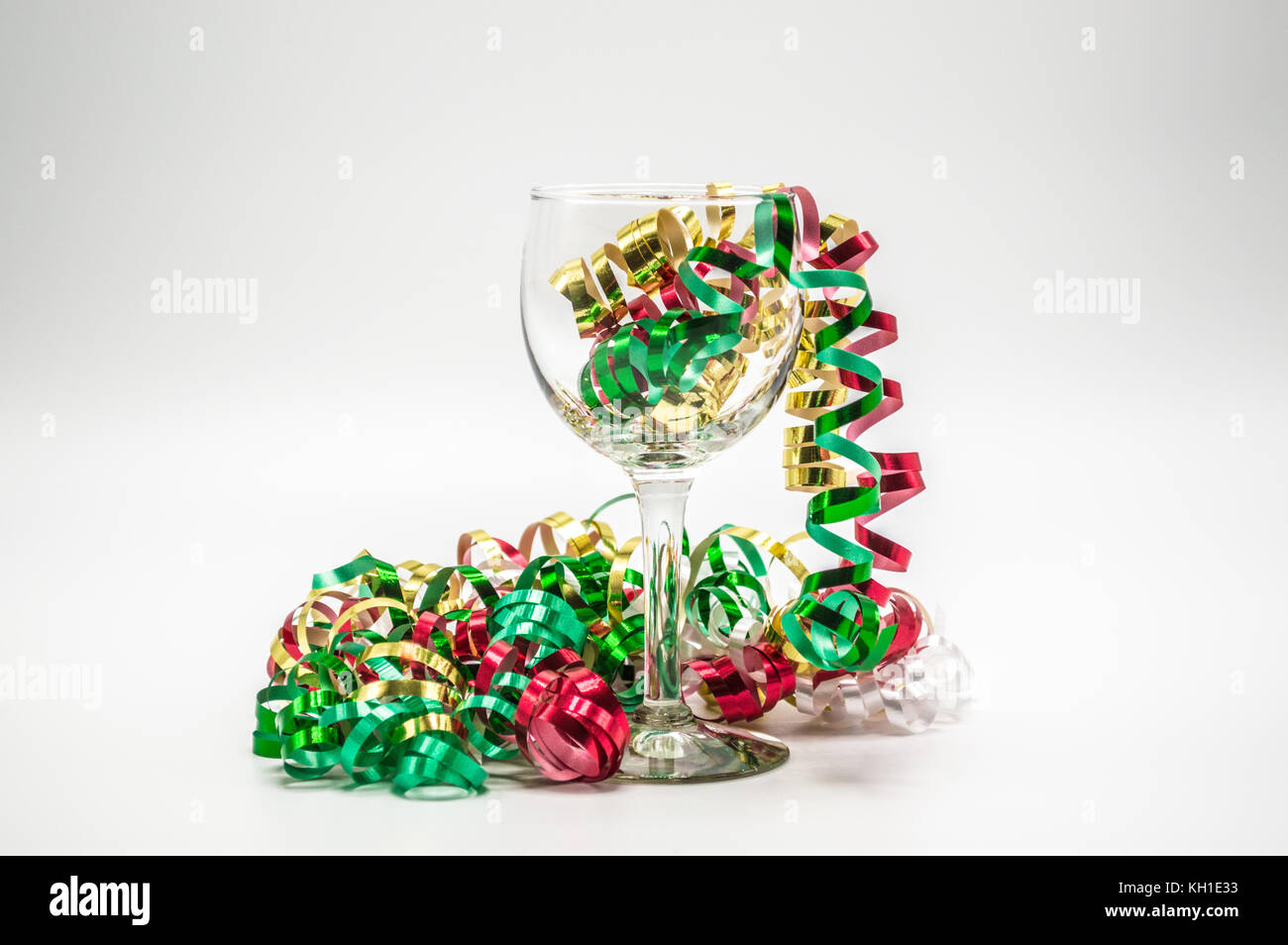 wine glass with colorful Christmas curling ribbon streaming out of it isolated on a plain background Stock Photo