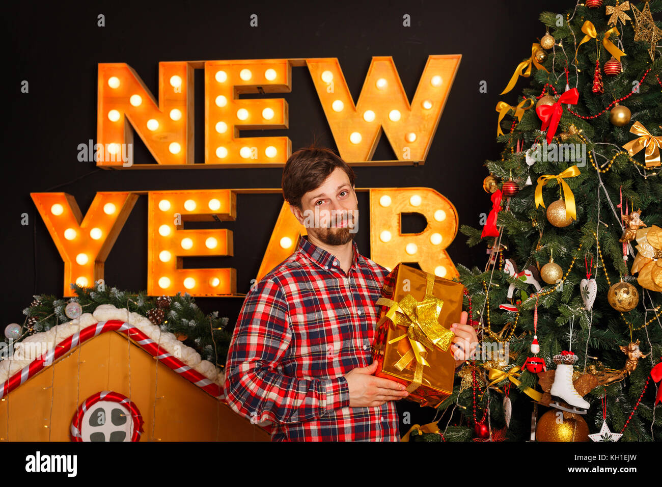 The guy is holding a Christmas gift and is standing by the tree. Merry Christmas and Happy New Year. Stock Photo