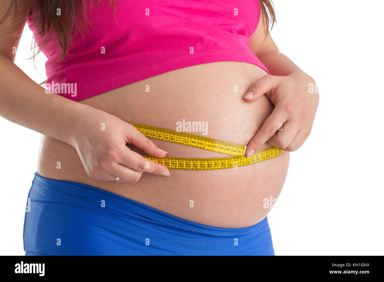 Pregnant female measuring tummy belly with yellow centimeter. Third trimester and meter, new life maternity concept. Stock Photo