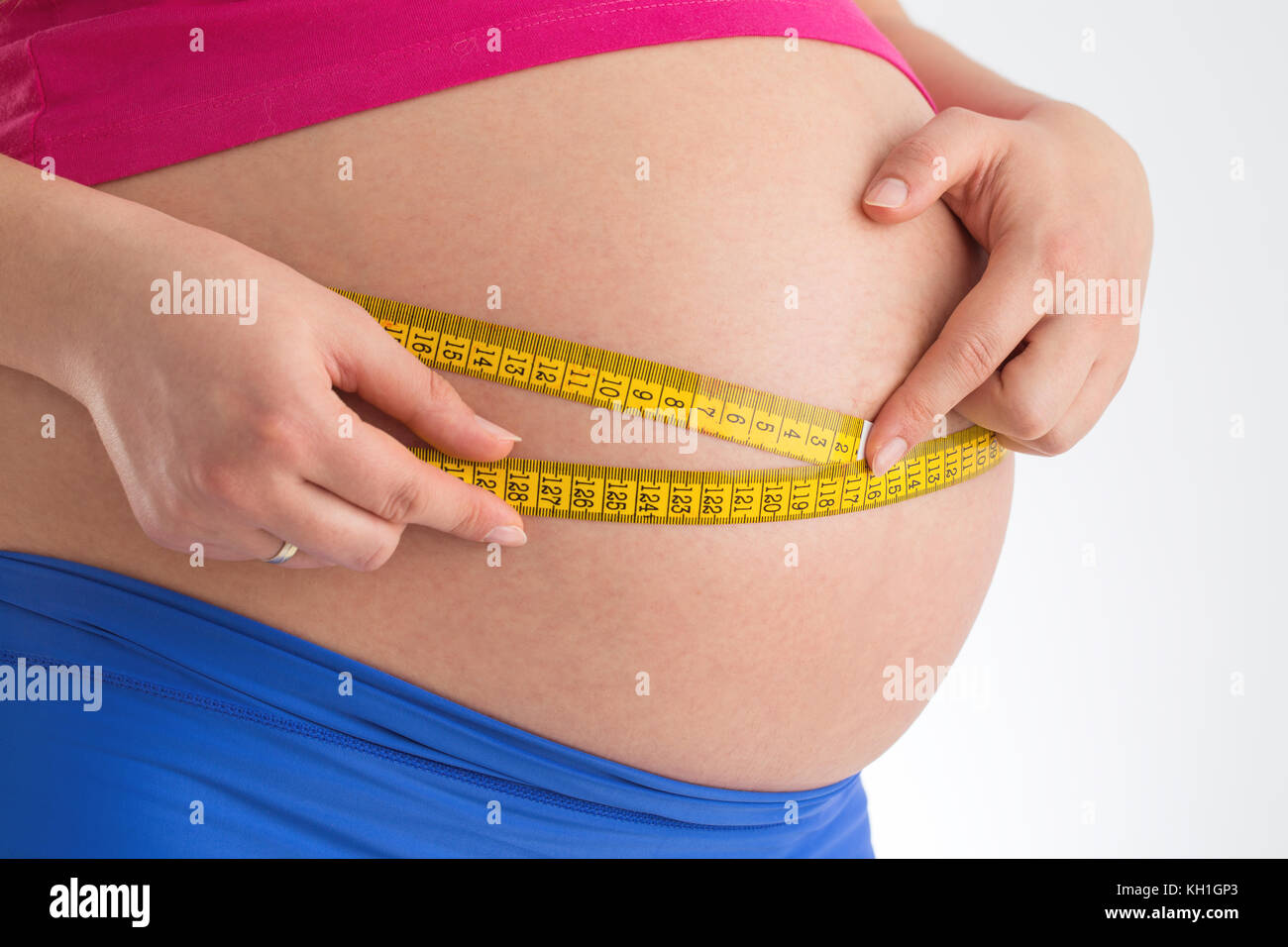 Pregnant female measuring tummy belly with yellow centimeter. Third trimester and meter, new life maternity concept. Stock Photo