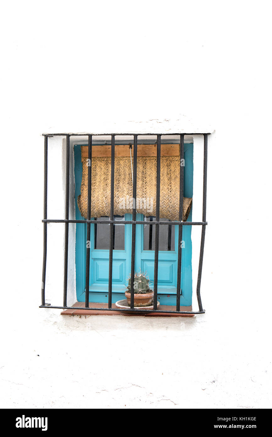 windows with wrought iron bars painted black with pots of red flowers on the windowsill and whitewashed wall Stock Photo