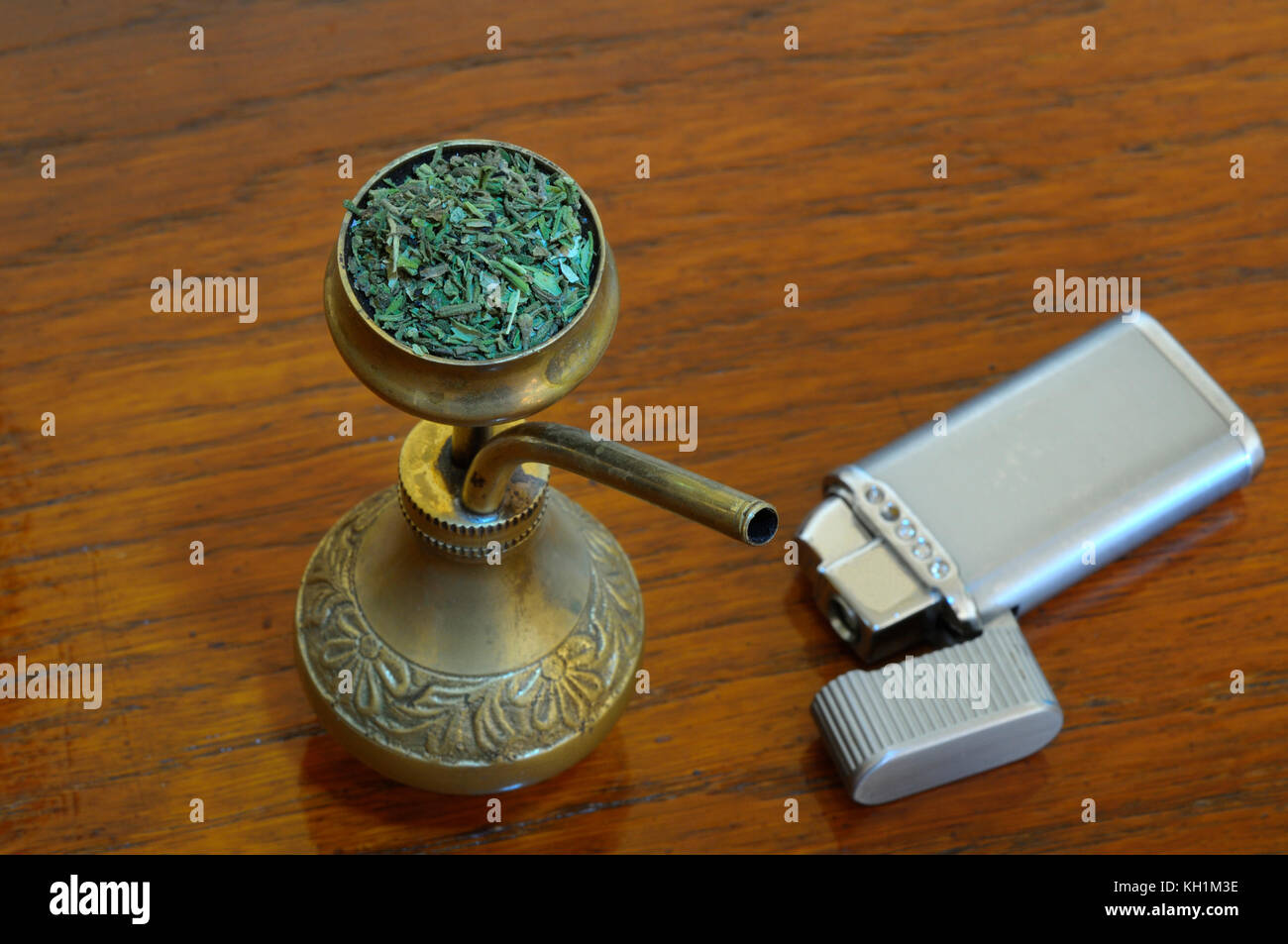 An old metal lighter and a brass bong with marijuana on it - placed on  wooden surface Stock Photo - Alamy