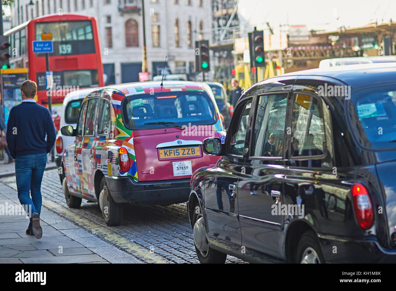 A man walking past a line of iconic London taxis waiting in the street. Stock Photo
