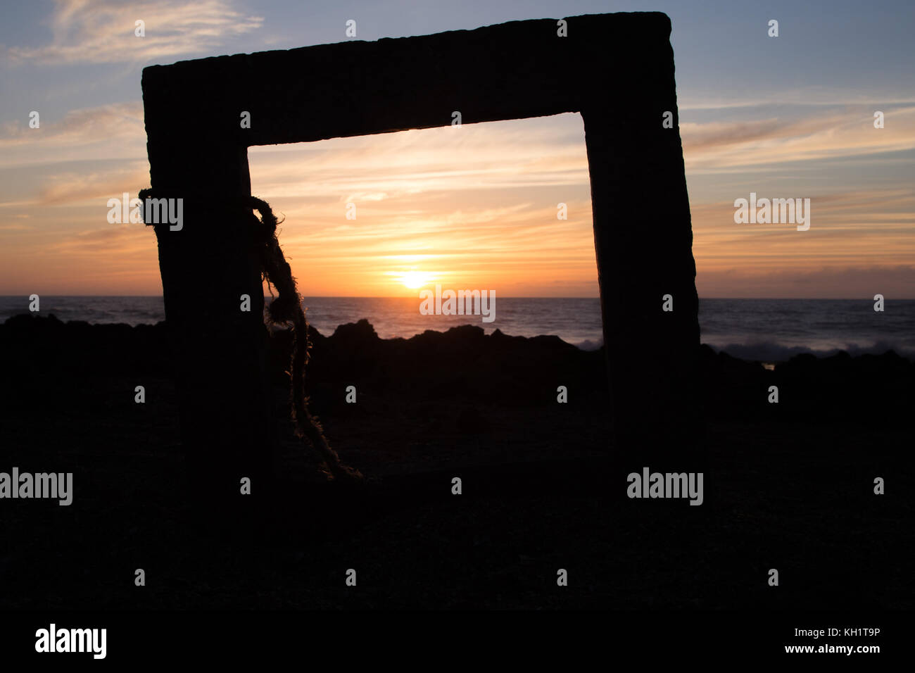 Orange sunset on a rocky coast through a concrete frame with a rope around it Stock Photo