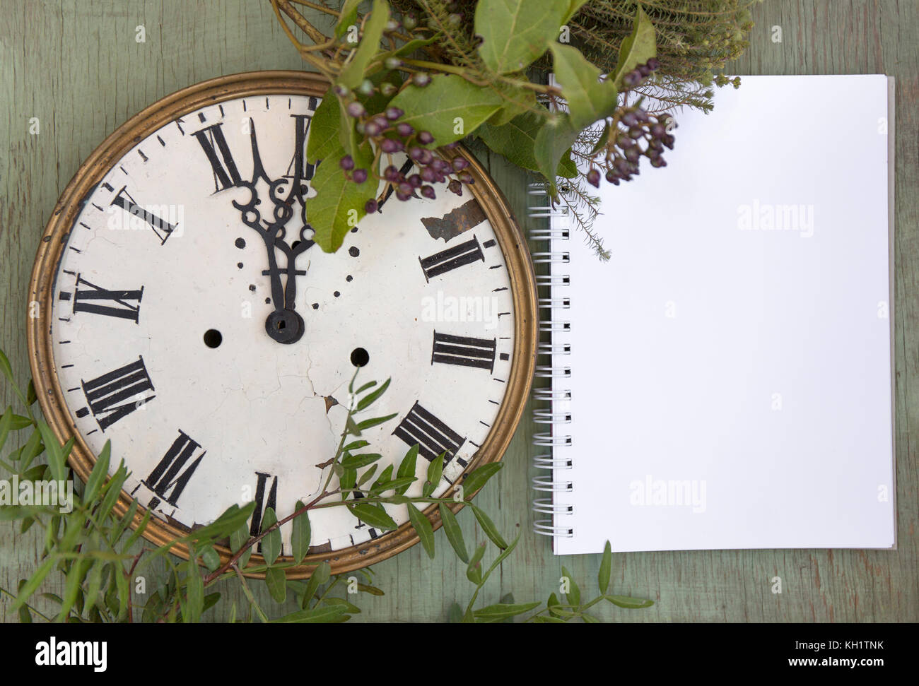 Old clock and blank notepad on the green wood background. New year ...