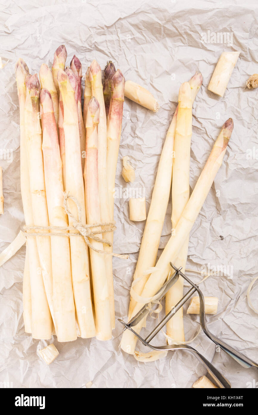 Bunch of white asparagus with peelings, on crumpled paper and metallic peeler. Stock Photo