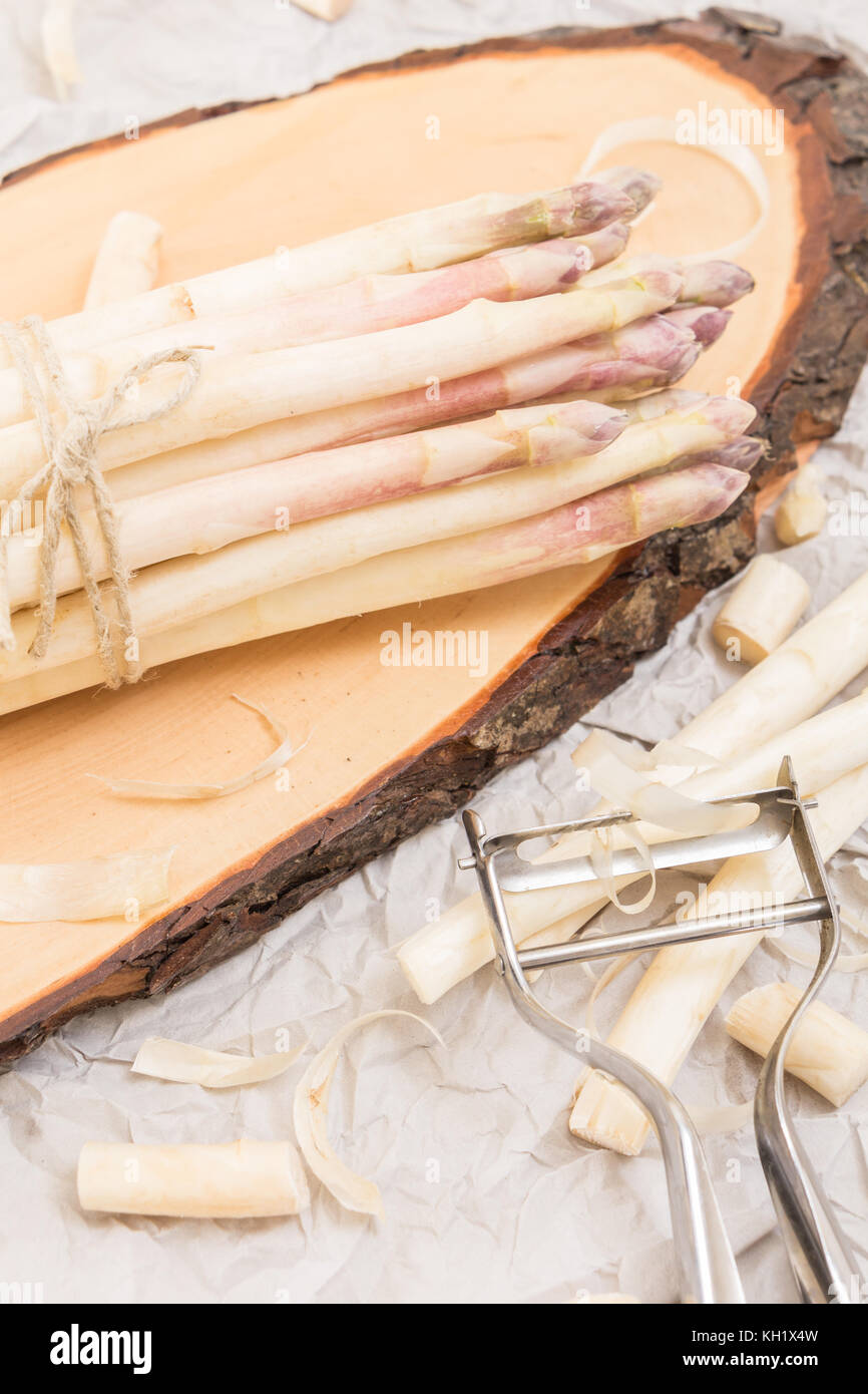 Bunch of white asparagus on  wood slice cutting board with metallic peeler,  on crumpled paper Stock Photo