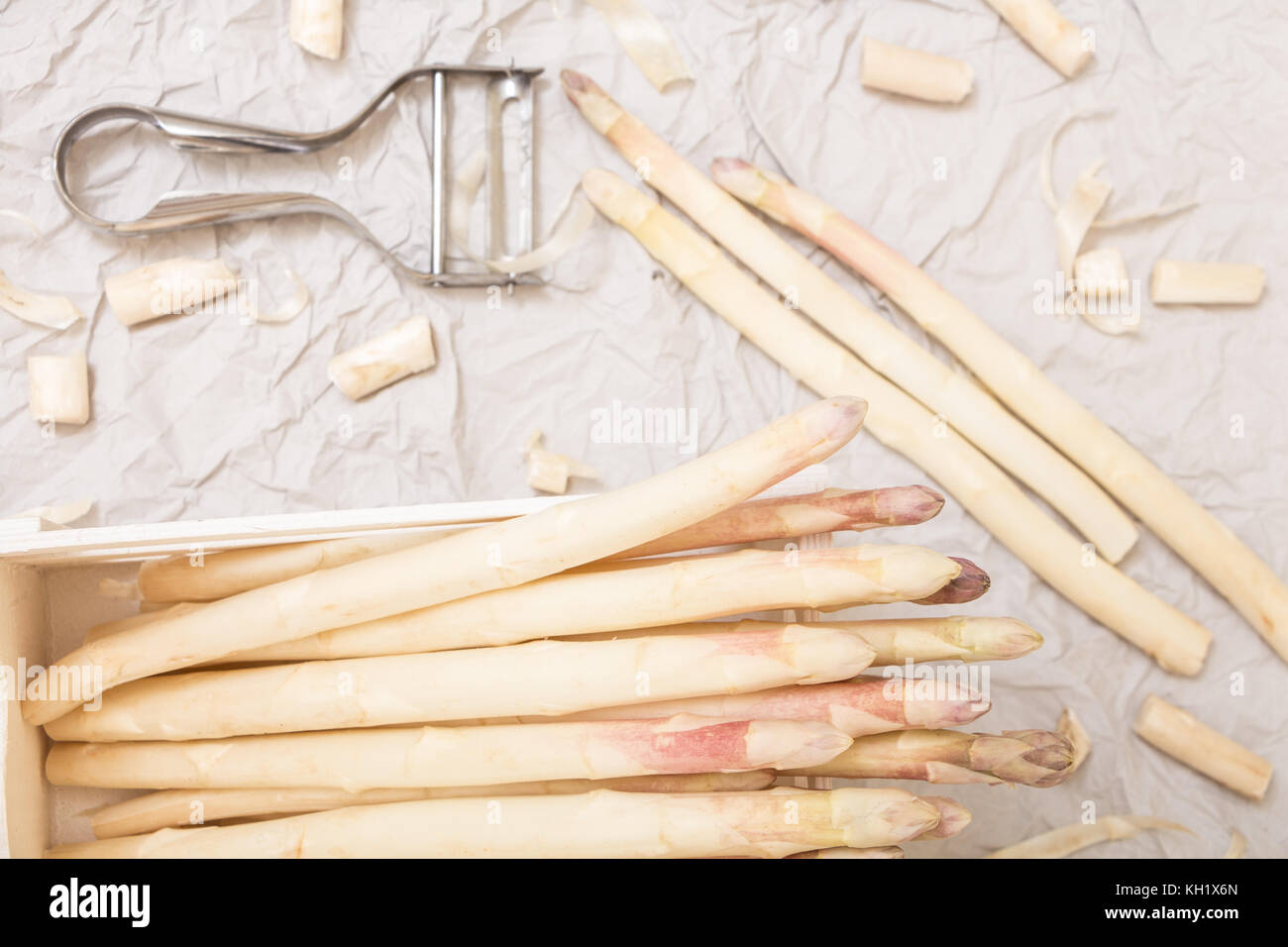 Bunch of white asparagus in box, on crumpled paper with metallic peeler. Stock Photo