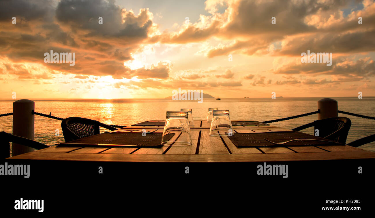 Table with glasses at restaurant with view of sunset, Indian Ocean, Republic of Seychelles. Stock Photo
