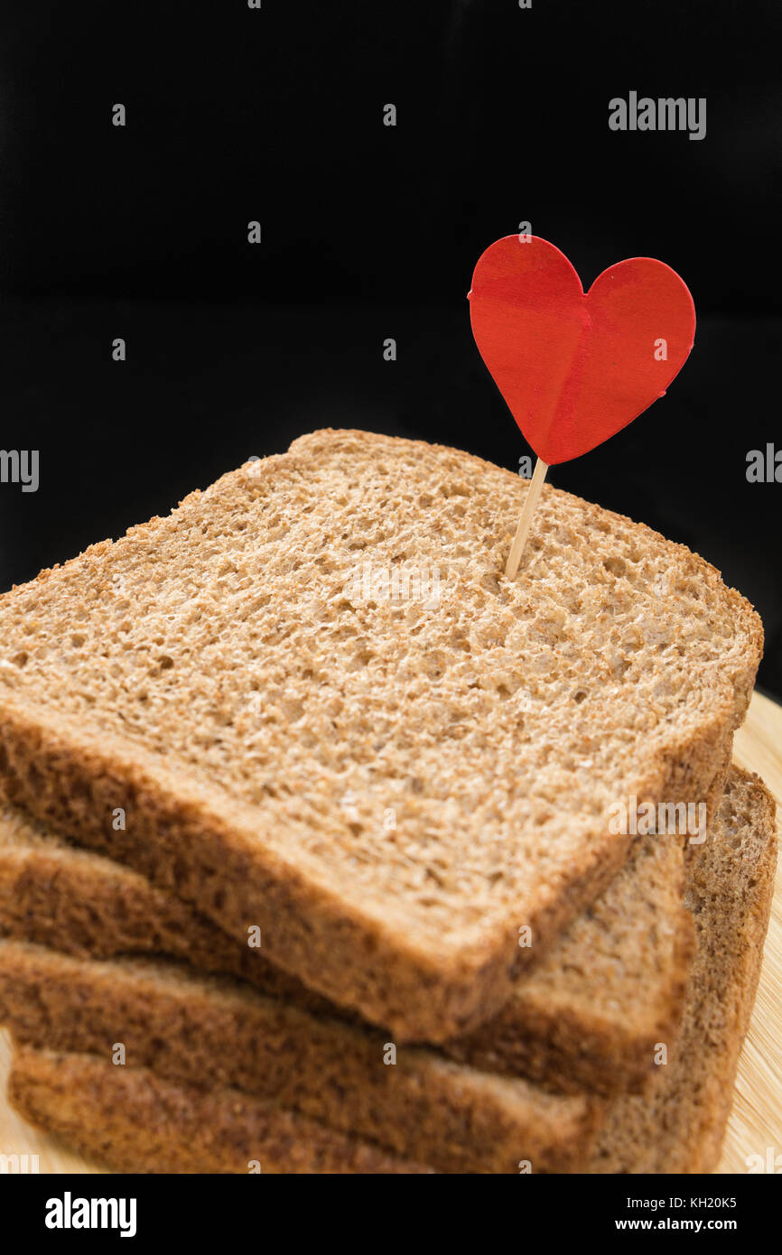 Whole grain sandwich bread slice with heart pin, with dark background
