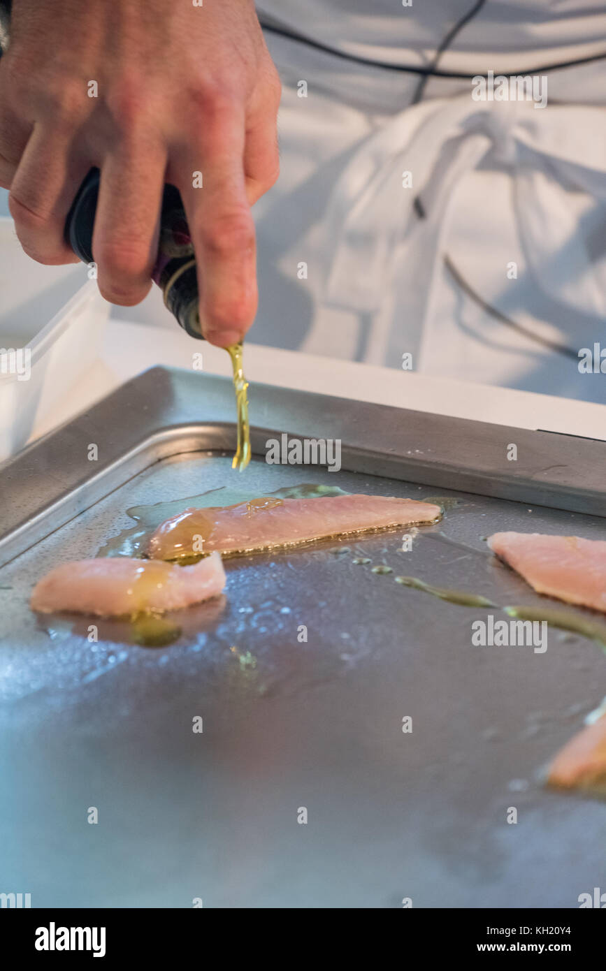 A chef pouring olive oil over a few fish fillets as they sear Stock Photo
