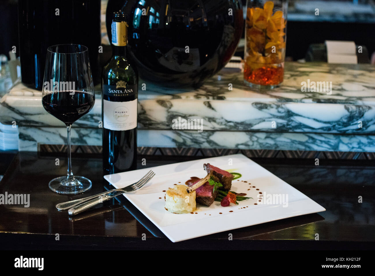 A lamb chop dish accompanied by a bottle and glass of red wine Stock Photo