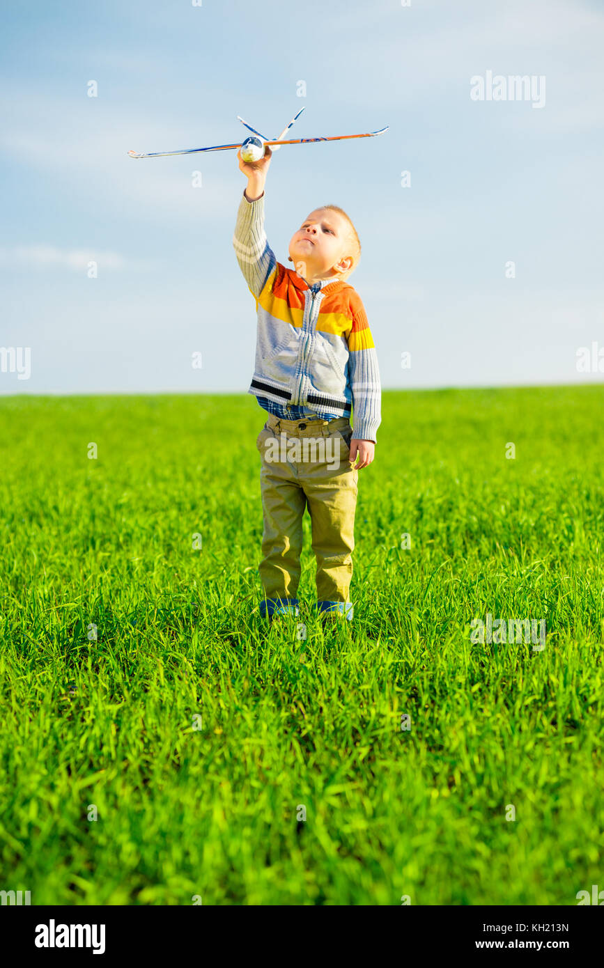 Happy kid playing with toy airplane against blue summer sky background ...