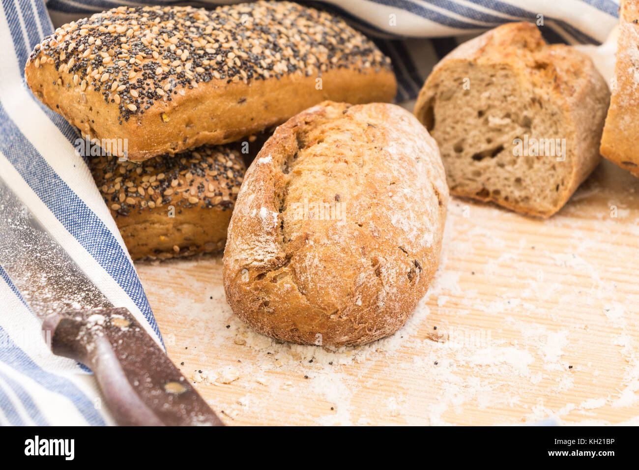 Whole wheat bread buns and slices, on wooden surface with flour Stock