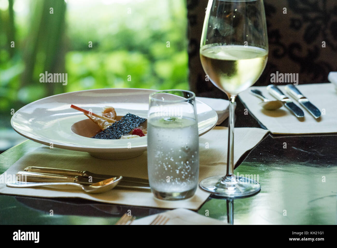 A seafood dish laid out on a dining table accompanied with a glass of chilled white wine and a glass of sparkling water with a lime. Stock Photo
