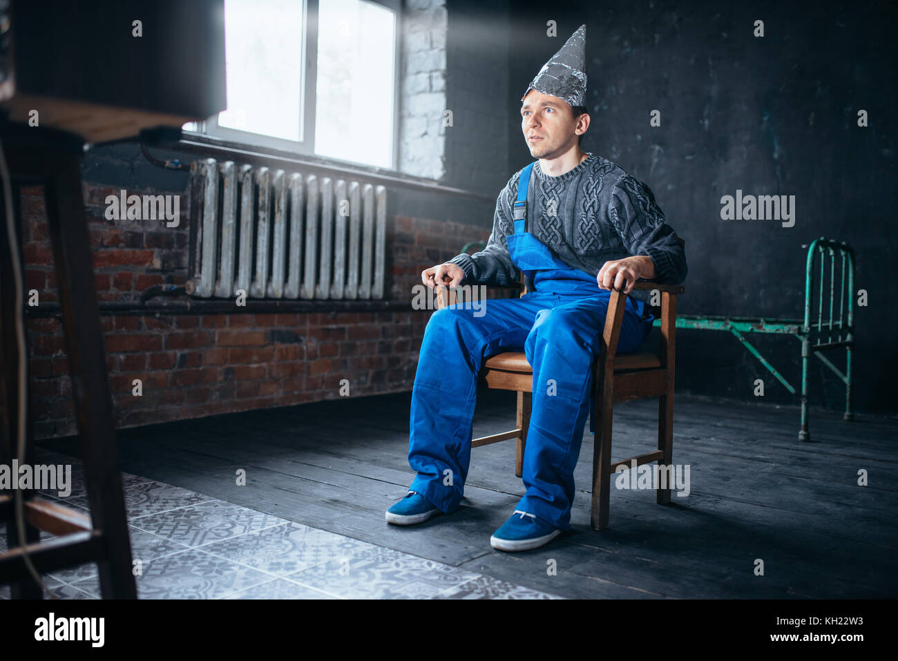 Afraided man in aluminum foil helmet sits in chair Stock Photo