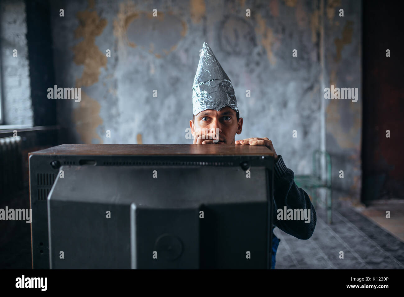 Afraid man in aluminum foil cap watch TV, UFO Stock Photo