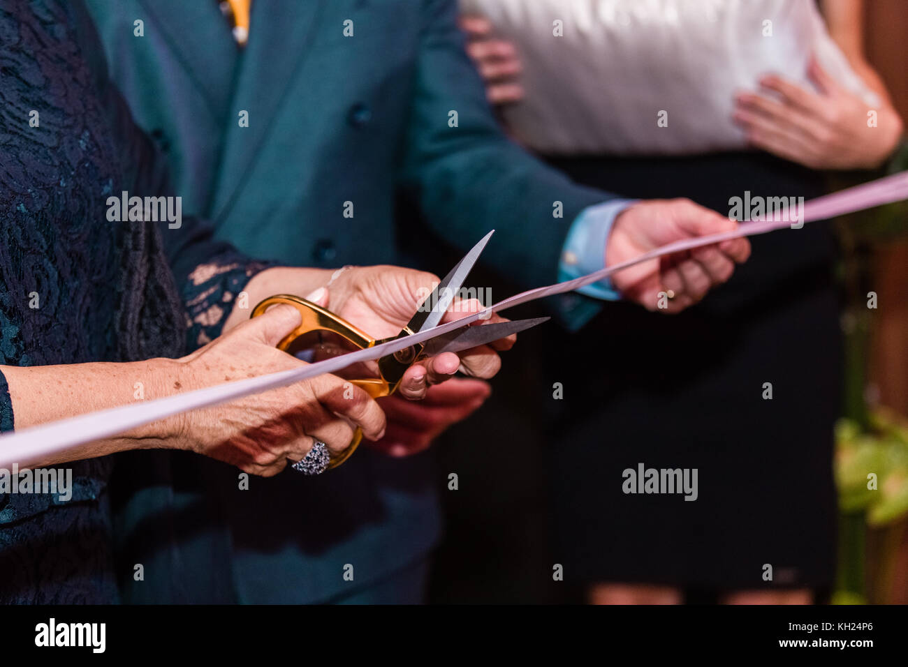 a woman holding scissors and cutting a pink ribbon during an opening ...