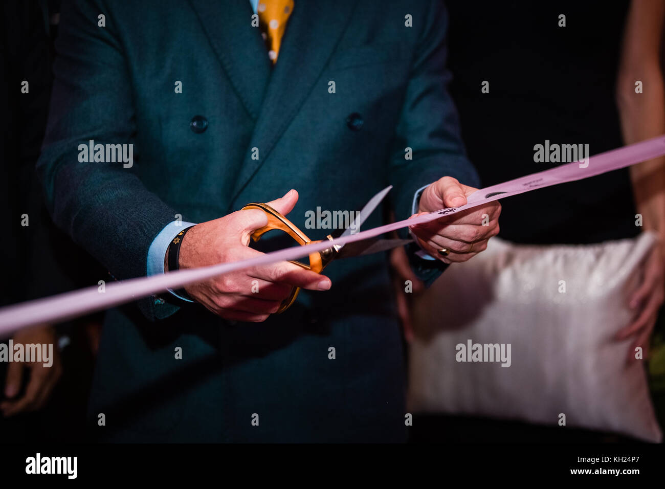 a man holding scissors and cutting a pink ribbon during an opening ceremony Stock Photo