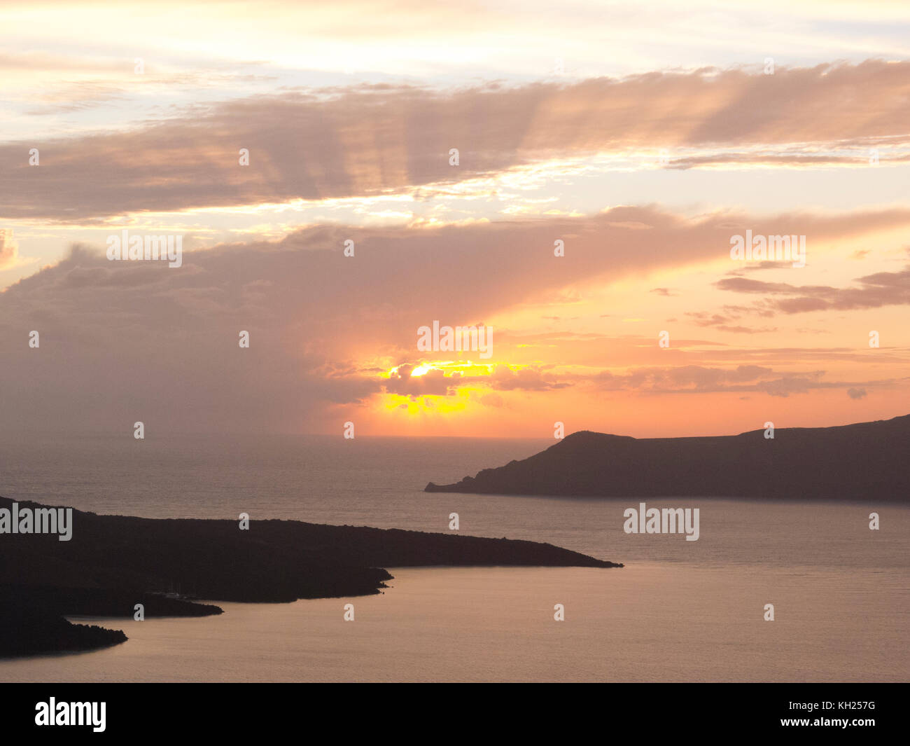 Setting sun over two landforms off the coast of Santorini, Greece, near the town of Oia Stock Photo